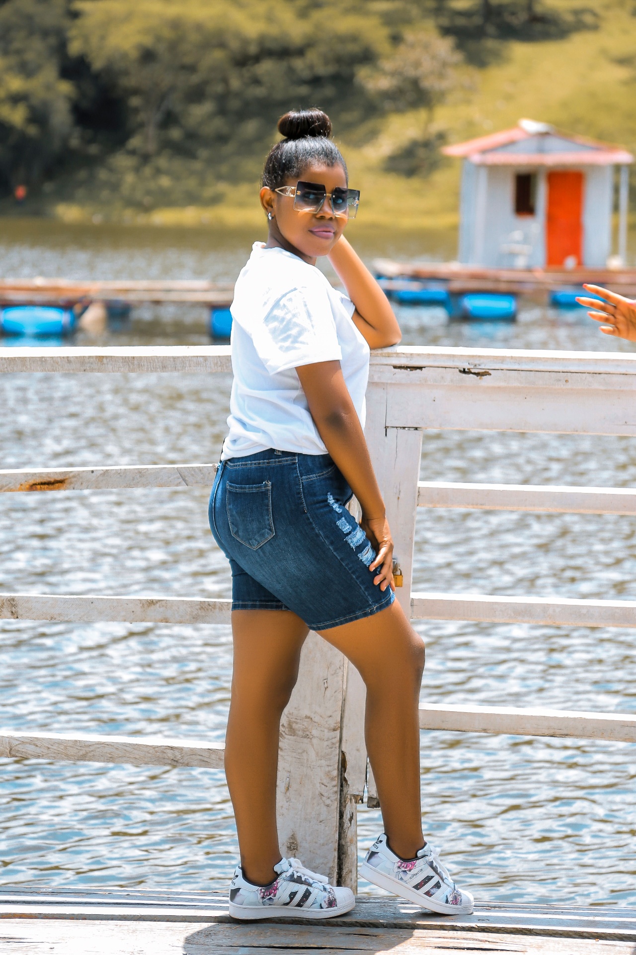 Woman in white tee and distressed mid-length denim shorts on a lakeside jetty