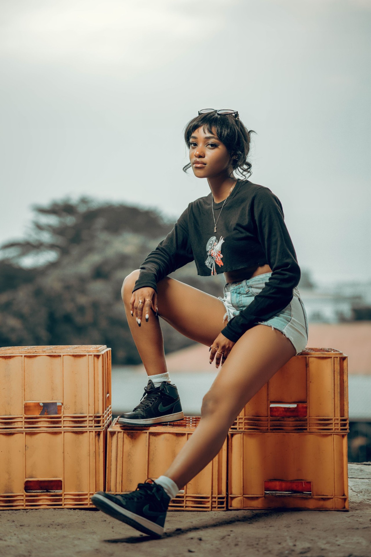 Woman in a black graphic long-sleeve cropped tee and denim shorts on crates