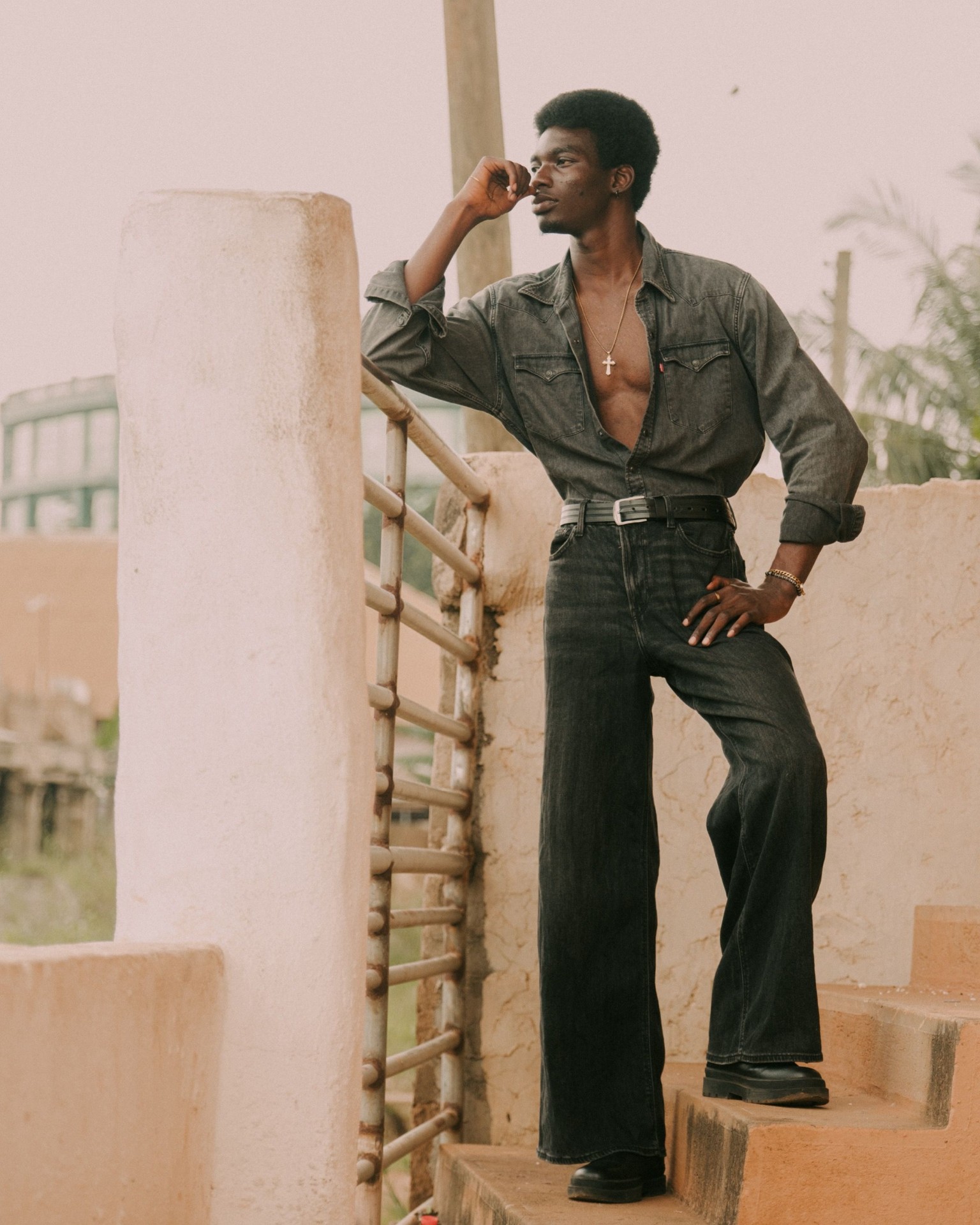 Man in a charcoal Western denim shirt with wide-leg black jeans on a sunlit rooftop