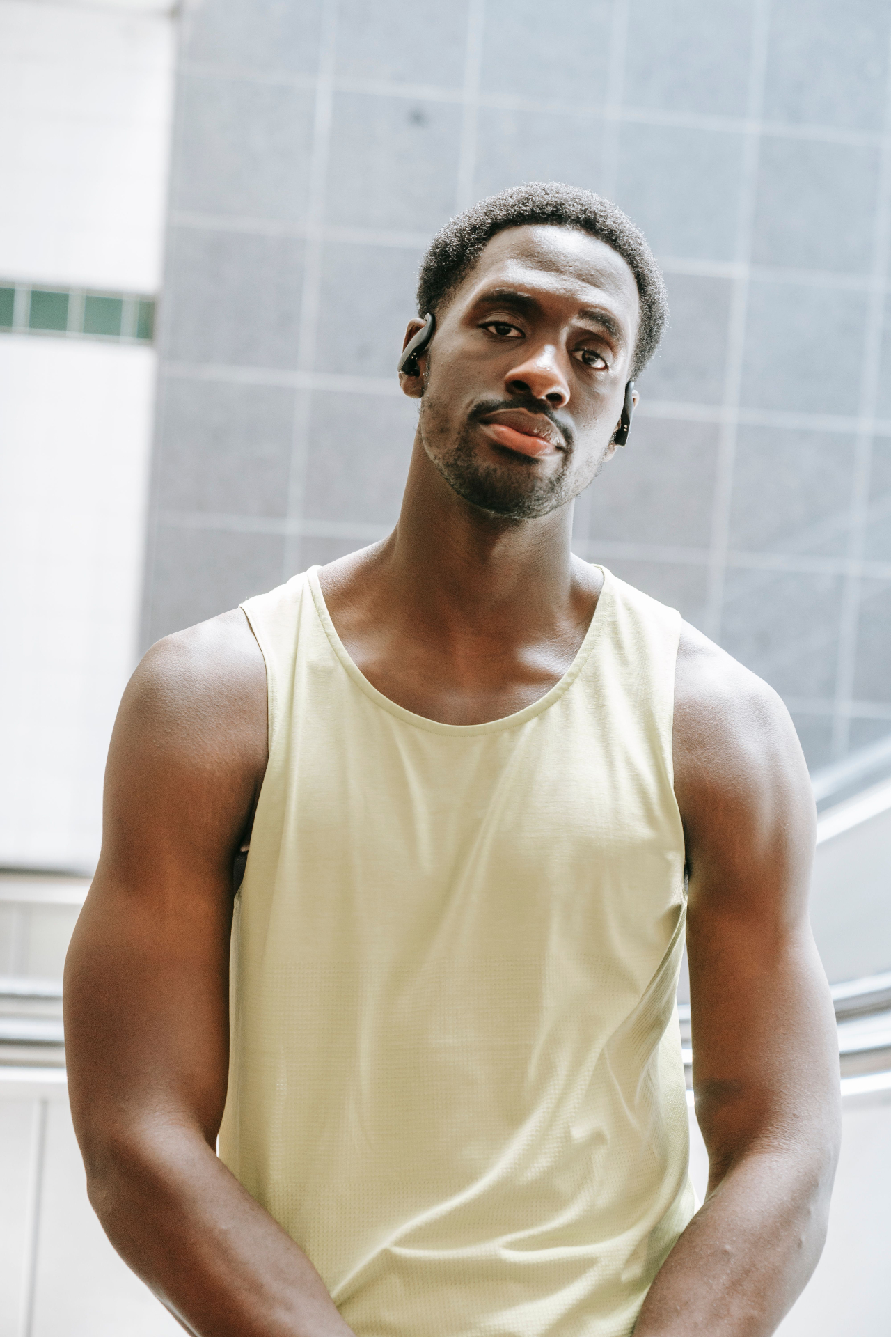 Man in pale yellow training tank with sport earbuds