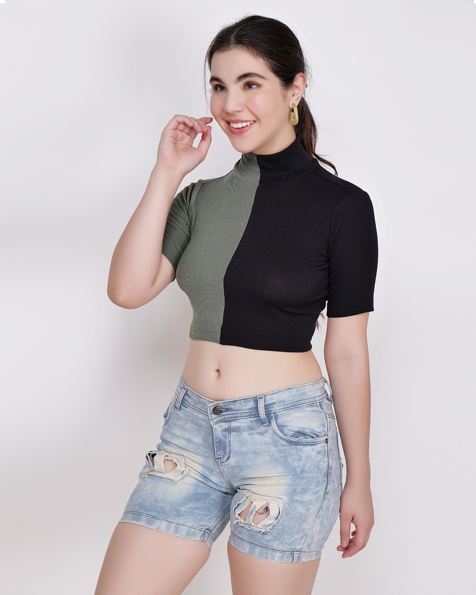 Woman in colour-block crop top and light acid-wash distressed denim shorts in studio
