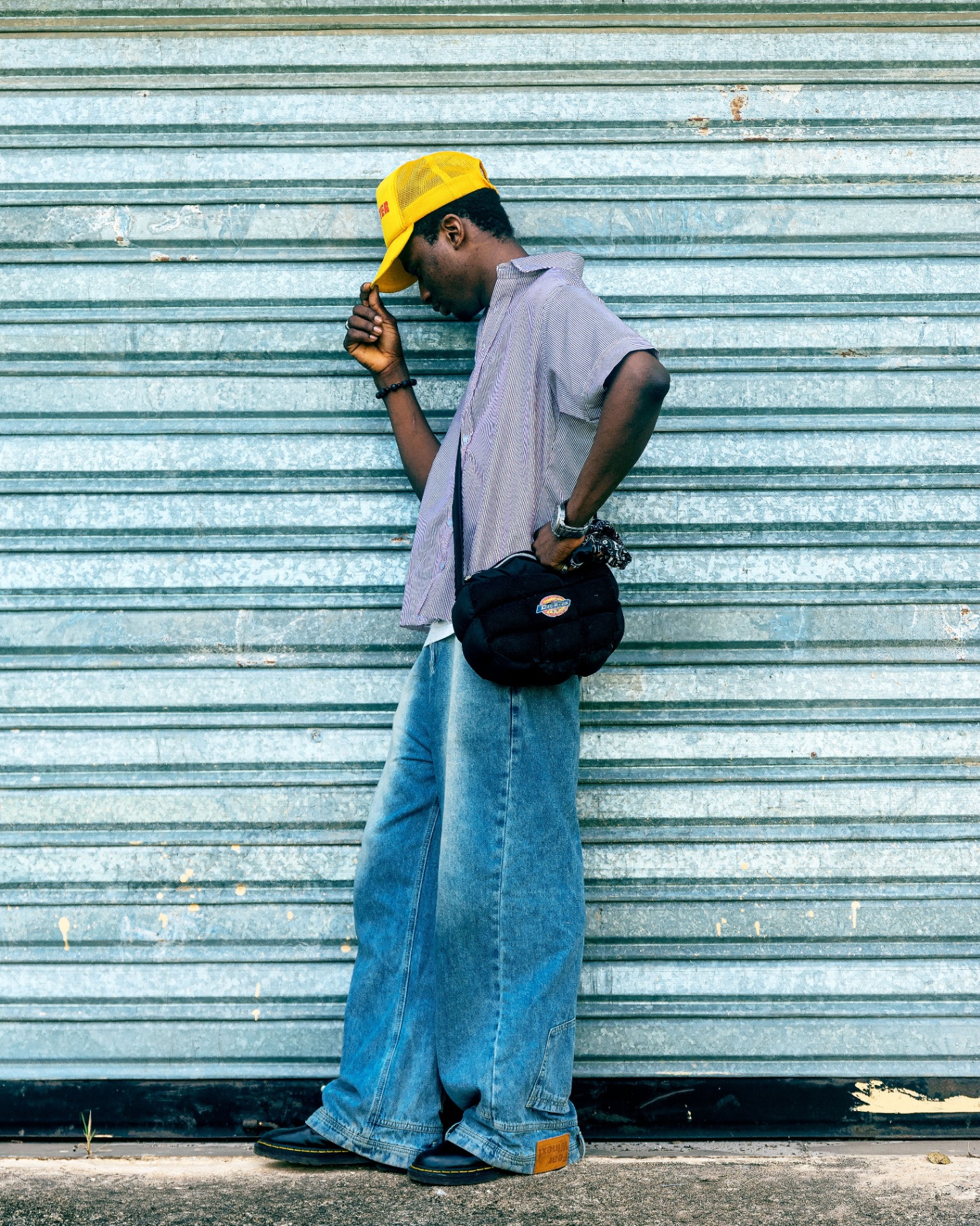 Man in a striped shirt and oversized baggy light-wash jeans against a metal shutter
