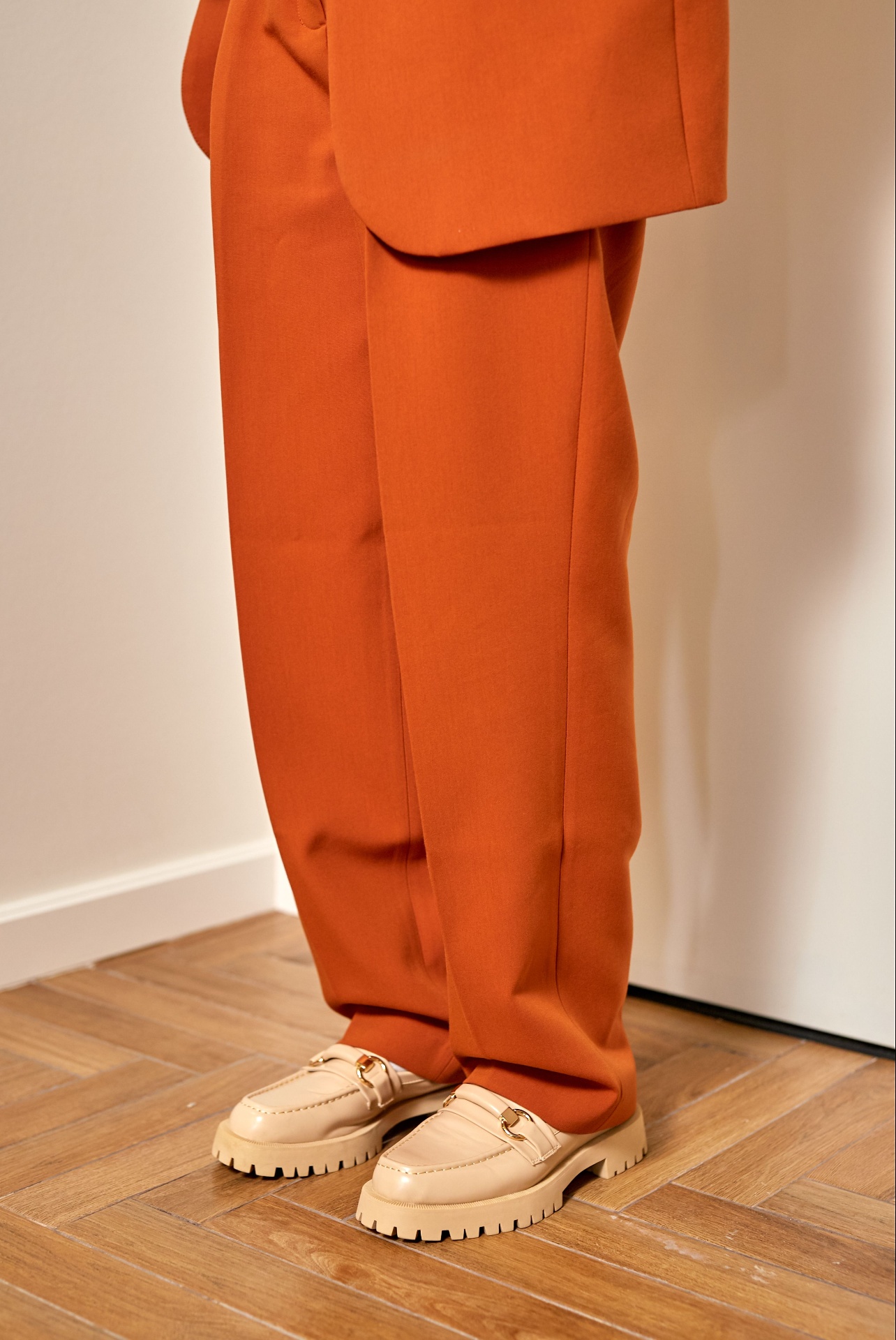 Detail of tailored rust orange wide-leg trousers with cream loafers on parquet