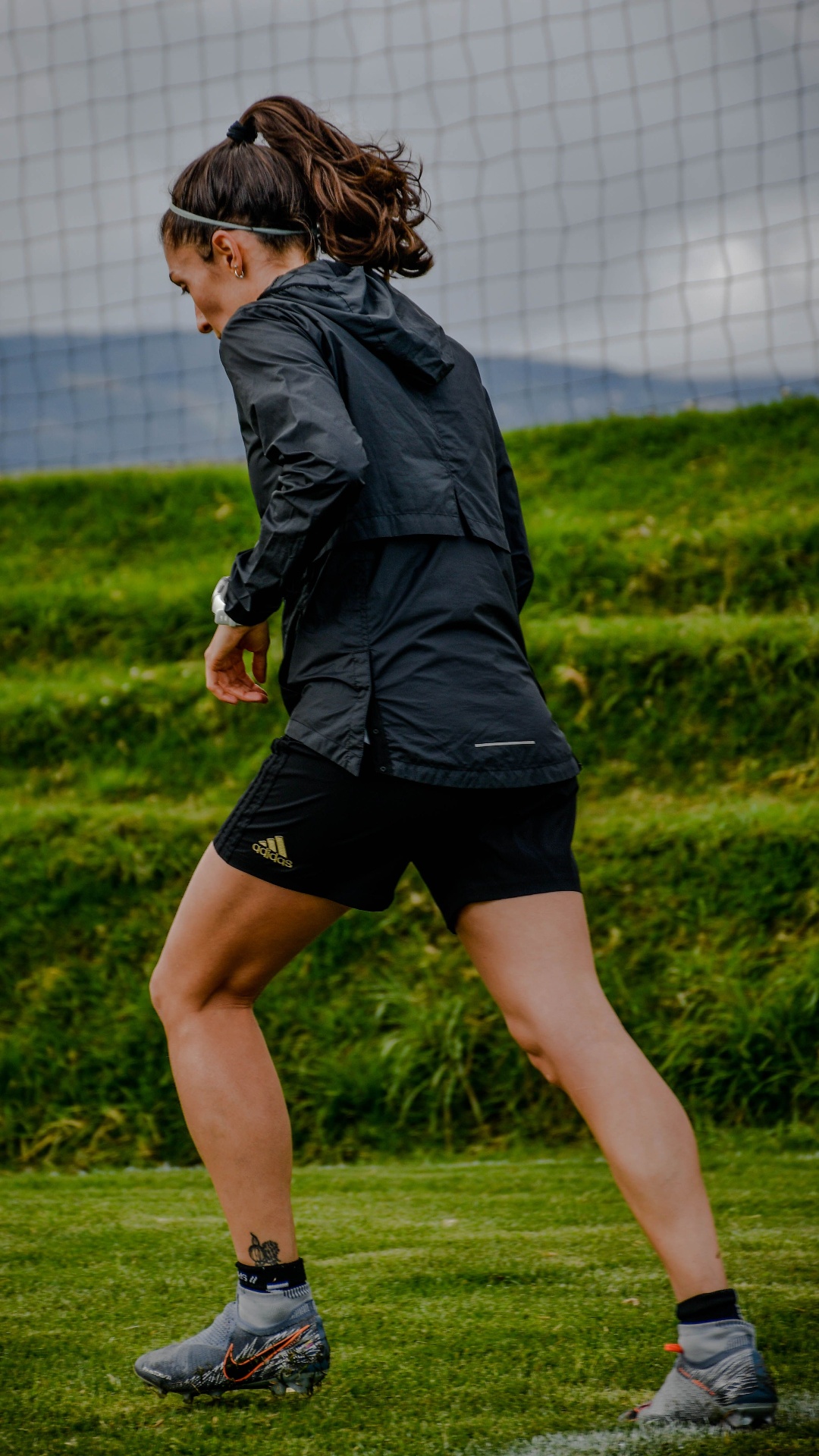 Athlete in black windbreaker and training shorts on a football pitch