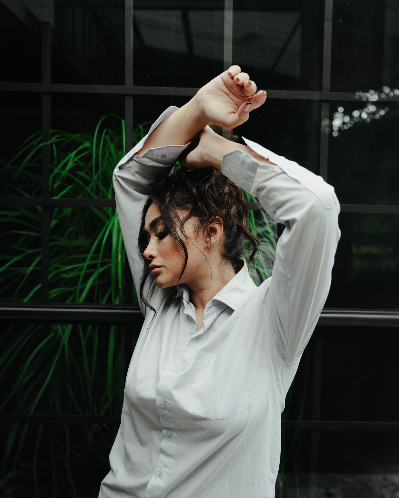 Woman in a crisp white button-down shirt posing outdoors by tall grasses and a dark window