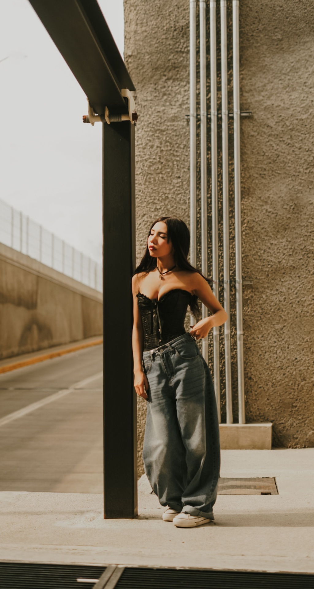 Woman in black corset and oversized baggy light-wash jeans on a sunlit street