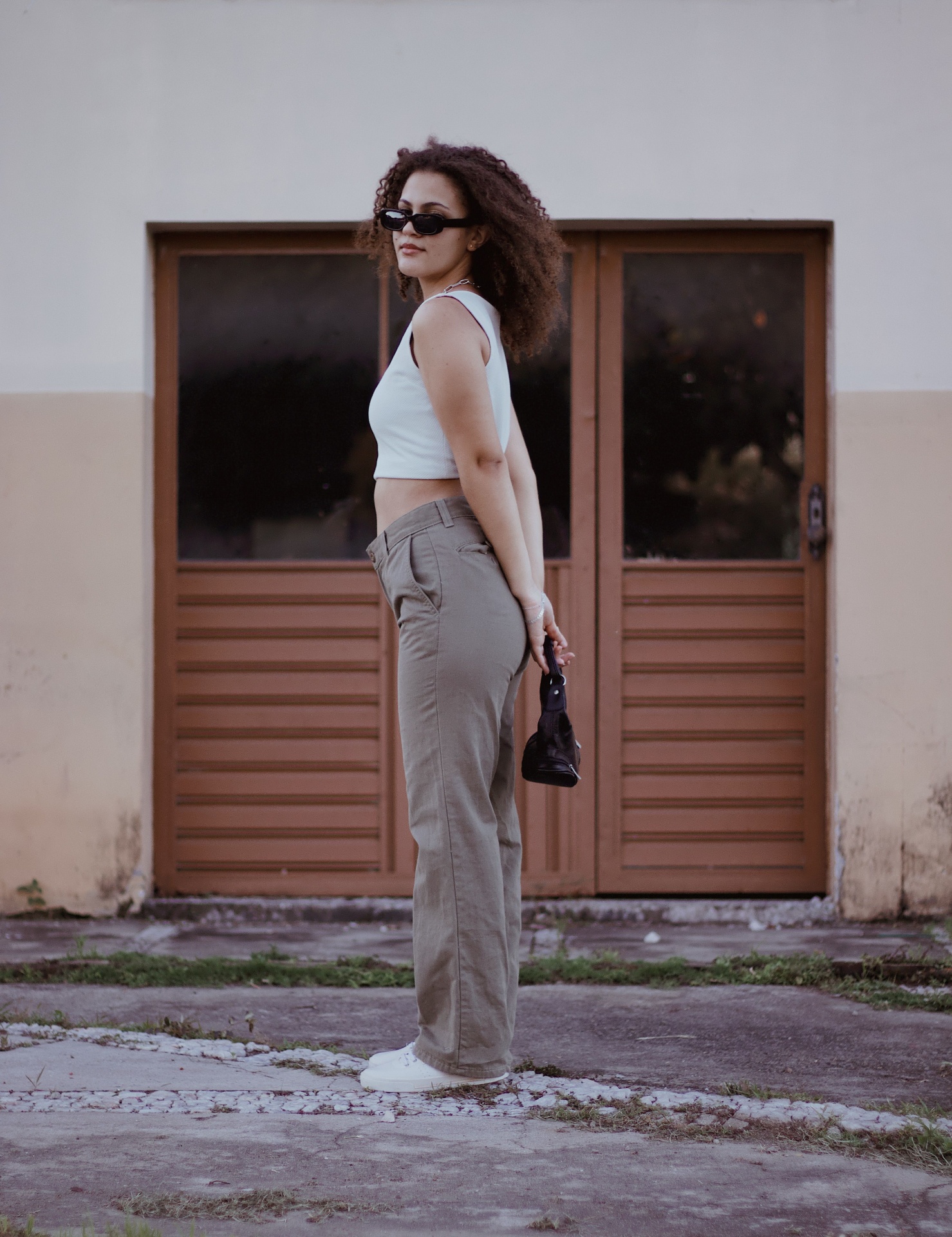 Woman in white ribbed tank and taupe straight-leg chino trousers by a wooden door