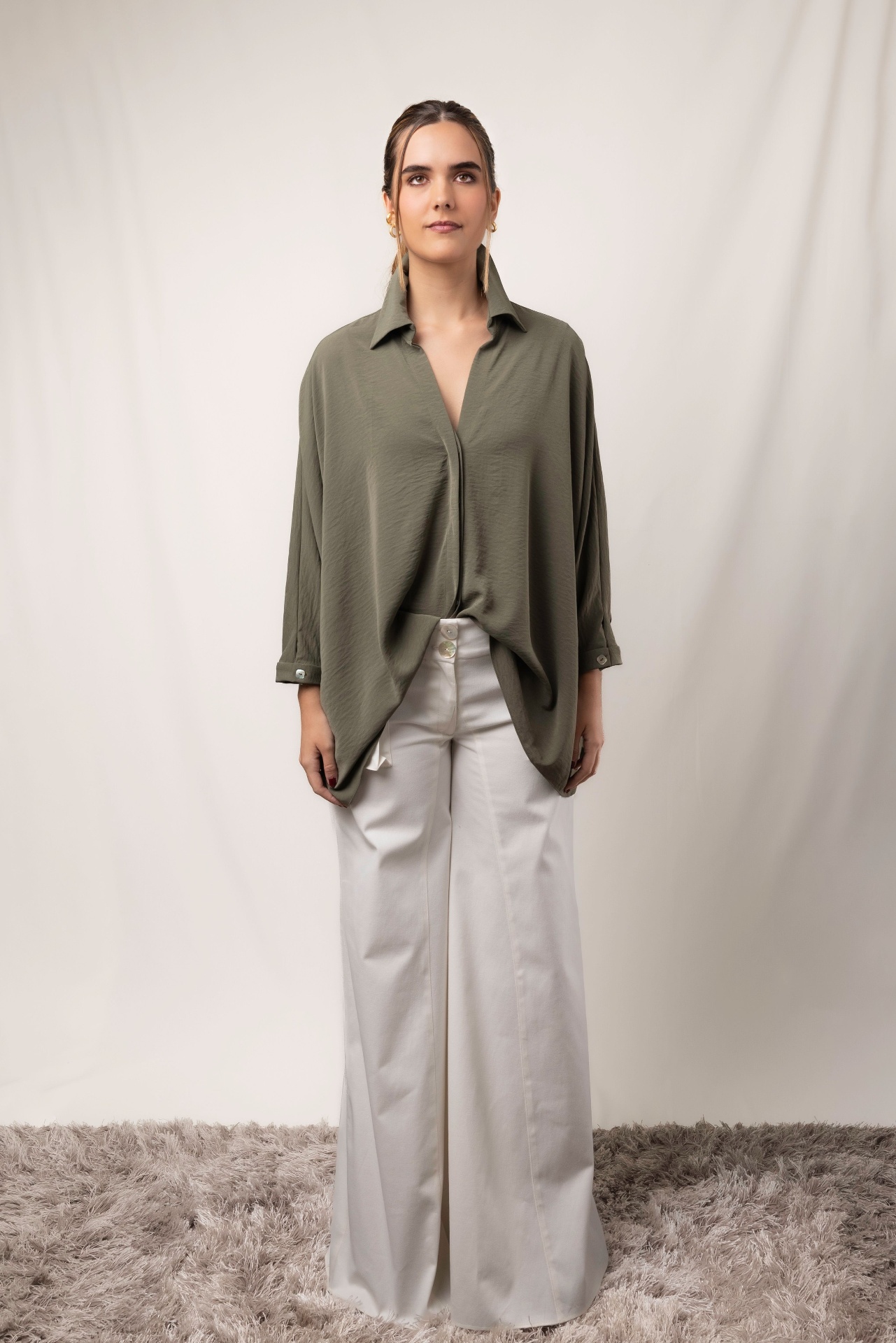 Woman in olive green oversized draped shirt and ivory wide-leg trousers in studio