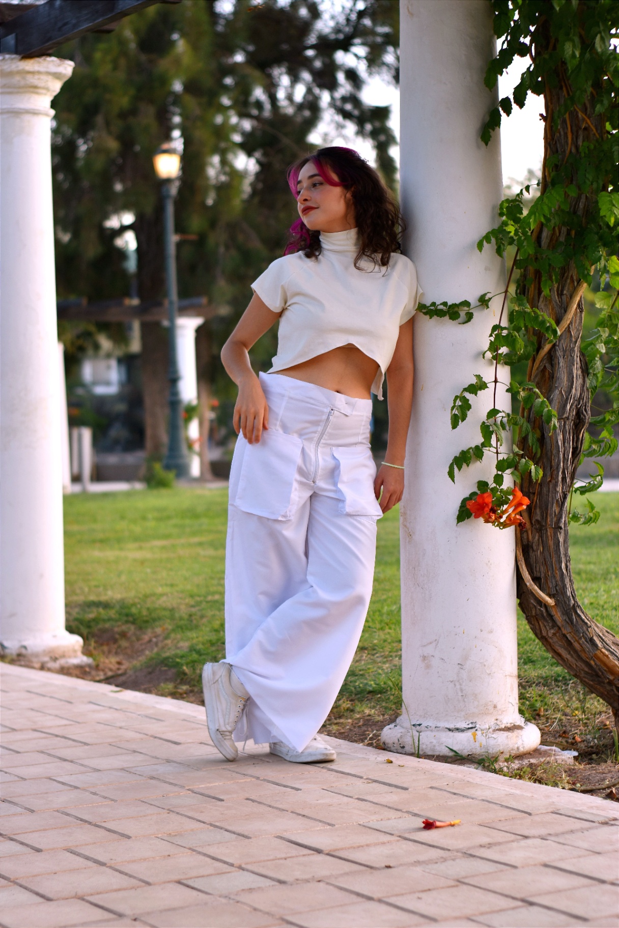Woman in cream mock-neck crop top and white wide-leg cargo trousers by a garden pergola