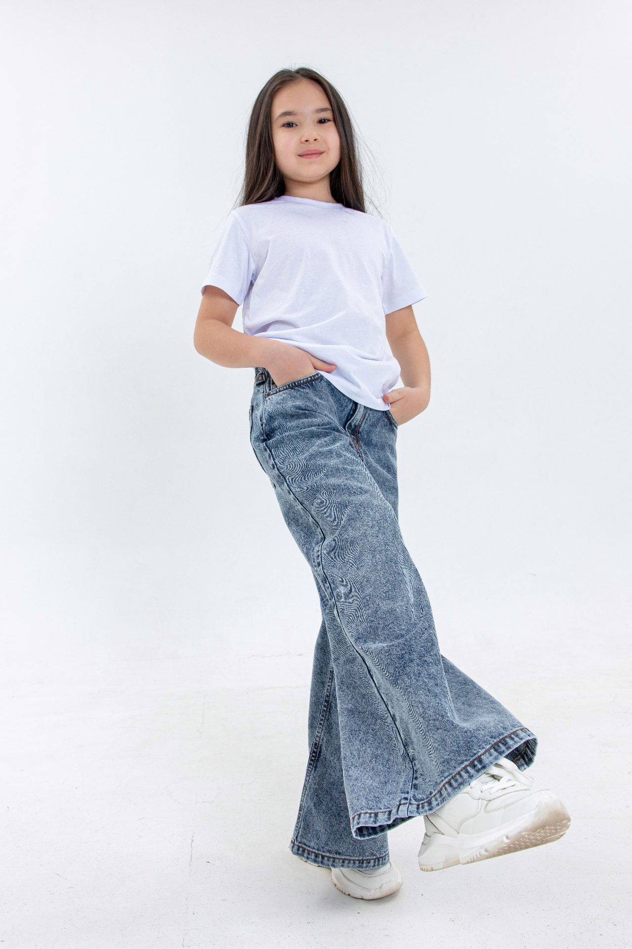 Young girl in white tee and acid-wash flared kids denim in a bright studio