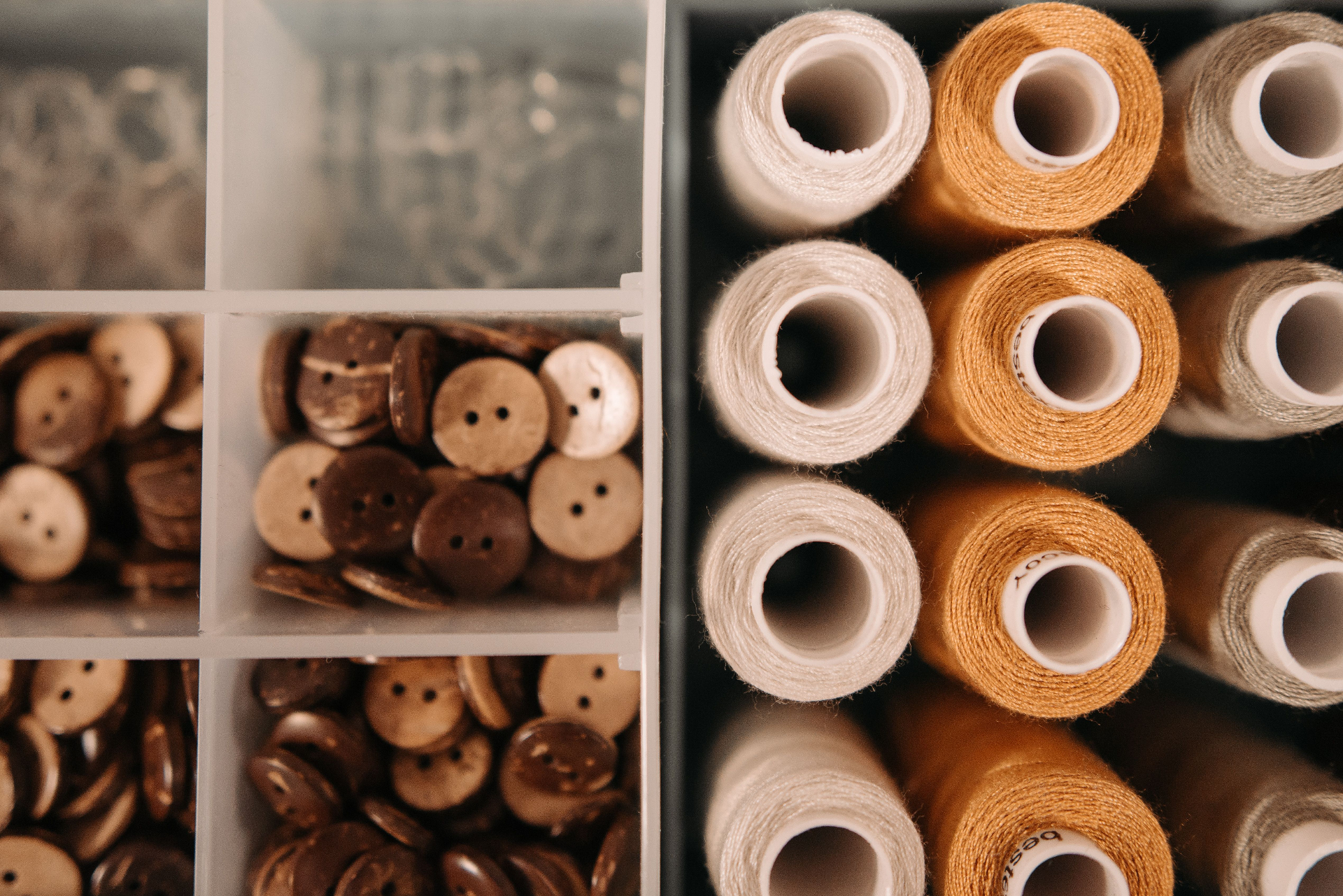 Wooden buttons and natural-fibre thread spools organised in a tray