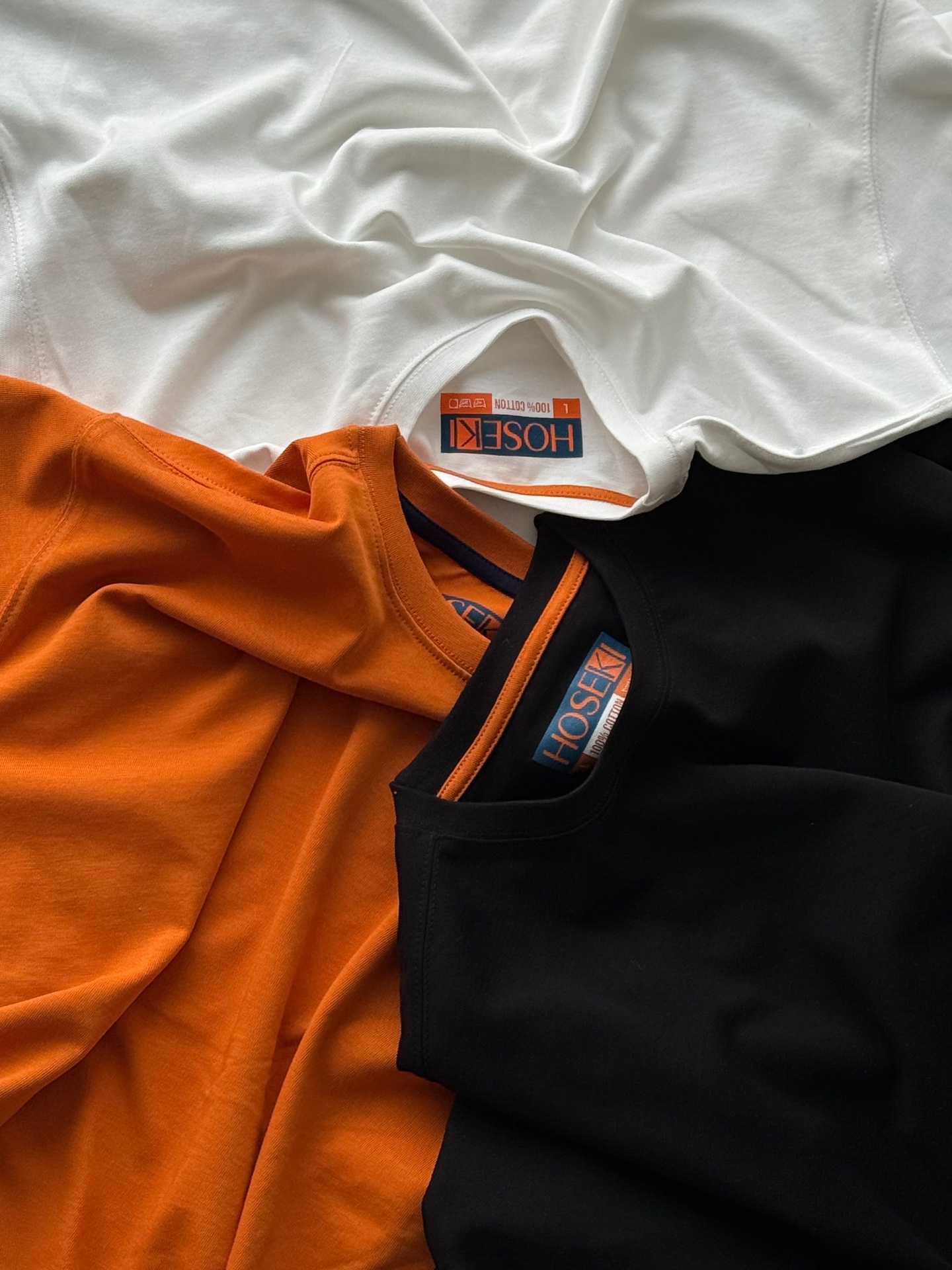 Folded white, orange and black cotton tees with brand labels